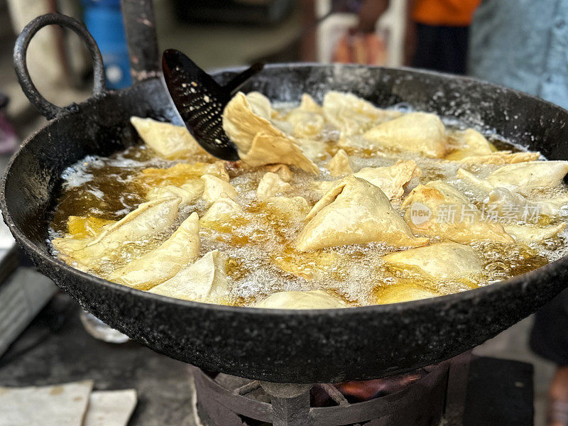 在karahi(印度炒锅)中油炸的一批samosas的特写图像，冒泡的热油，开槽的勺子，印度街头小吃摊，不健康的饮食，重点放在前景