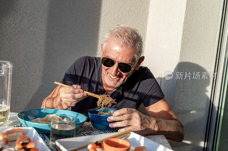 有魅力的中年男子一边吃一边开心地坐在桌子旁摆放着中餐外卖