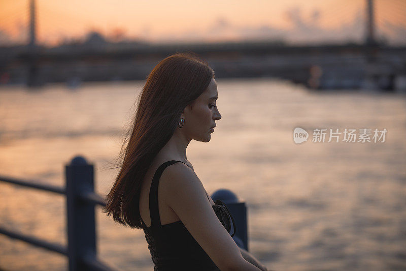 身穿黑色连衣裙的年轻美女在伊斯坦布尔的加拉塔桥上欣赏日落