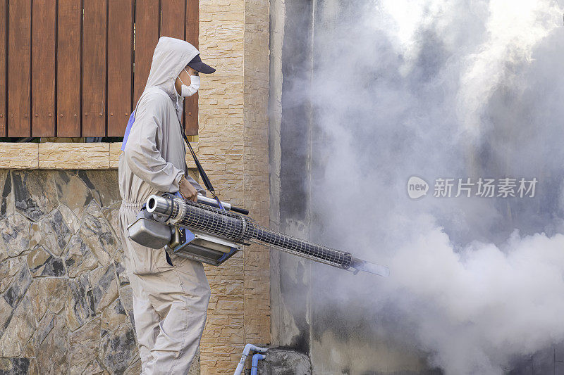 户外卫生工作者利用喷雾机喷洒化学药剂，在房屋围栏旁的废弃区域消灭蚊虫，控制登革热疫情