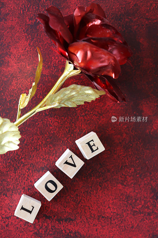自制DIY简易情人节卡片设计的特写图像，除了红色和金色金属外，白色字母骰子拼写“爱”，模型玫瑰在斑纹的红黑色背景上，手工制作的浪漫贺卡，抬高视图