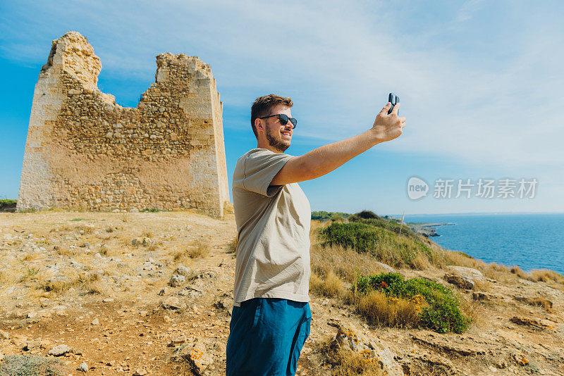 男子旅行者用智能手机拍摄意大利普利亚波尔图塞尔瓦吉奥国家公园的老堡