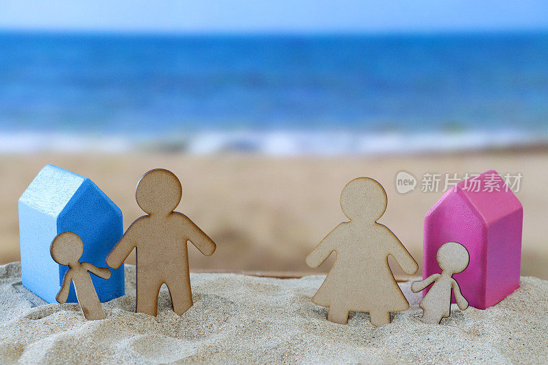 木雕分离家庭的特写图像，蓝色和粉红色的沙滩上的木制模型度假小屋，父母和孩子，父亲和儿子，母亲和女儿，沙滩背景，海浪在退潮时破碎，海岸线，离婚家庭度假