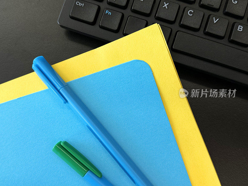 蓝色和黄色的纸上写着制造商或笔，模糊焦点的计算器放在办公桌上。