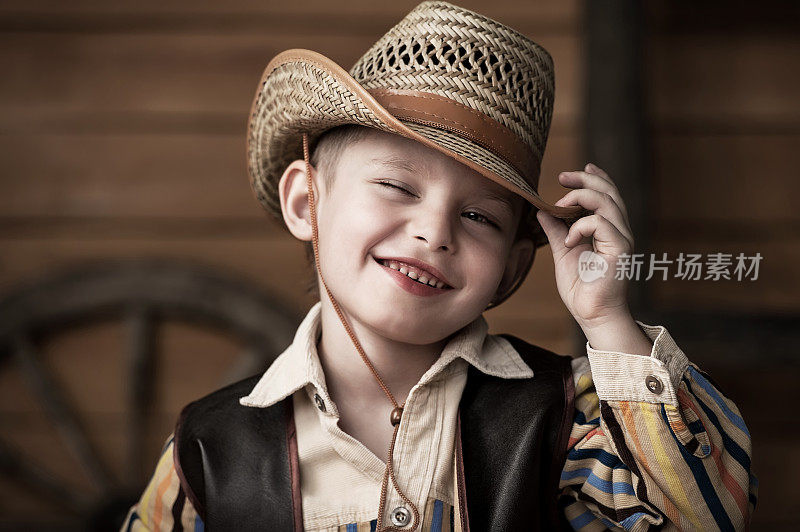 一个小男孩戴着牛仔帽，穿着牛仔装微笑着