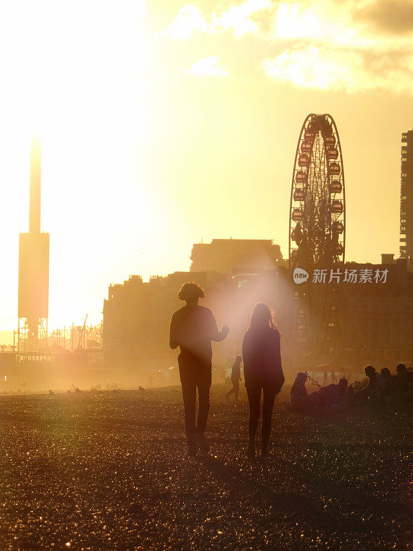 一对夫妇漫步在布莱顿海滩上，夕阳下骑着大轮子