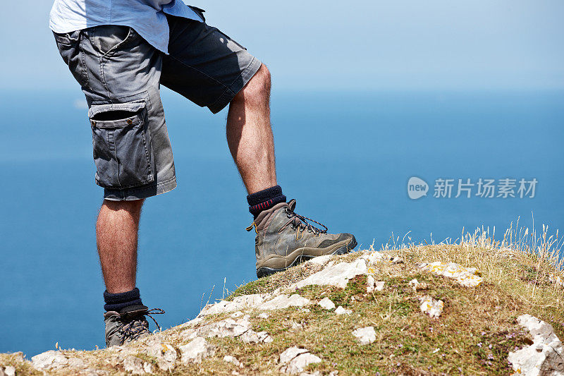 成熟的白人男子站在悬崖上的靴子和腿特写