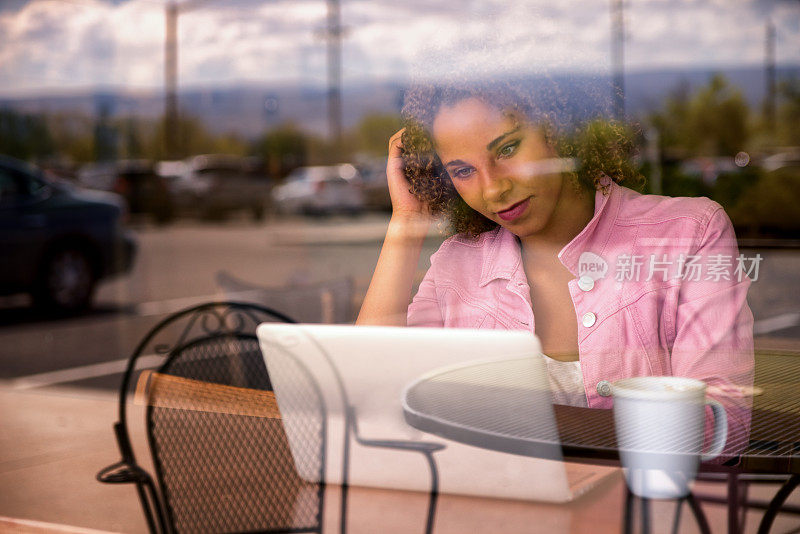 漂亮的混合种族年轻女子使用笔记本电脑通过窗口视图