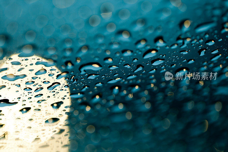 雨点落在挡风玻璃上，车头灯在背景中