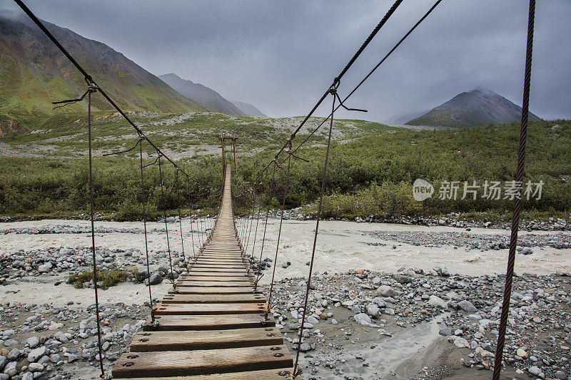 木制悬索桥横跨一条流淌的河流在阿尔