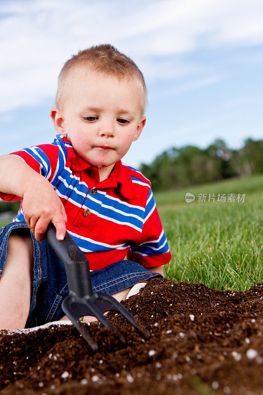 蹒跚学步的小男孩在花园里挖土