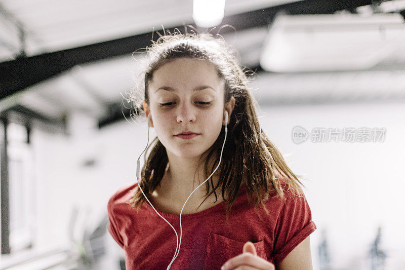 年轻女性在跑步机上跑步，还戴着耳机