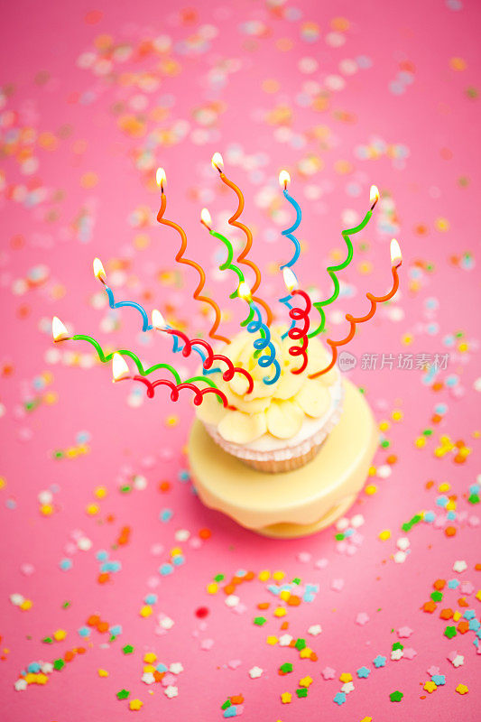 生日纸杯蛋糕，粉红背景上有蜡烛和五彩纸屑