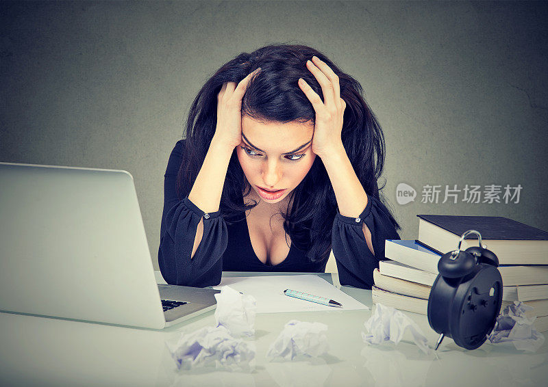 太多工作压力的女人坐在她的书桌前，在笔记本电脑前看书
