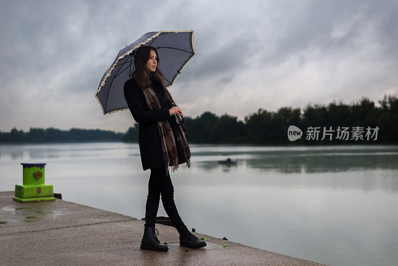 一名年轻女子在雨中撑着伞站在码头上