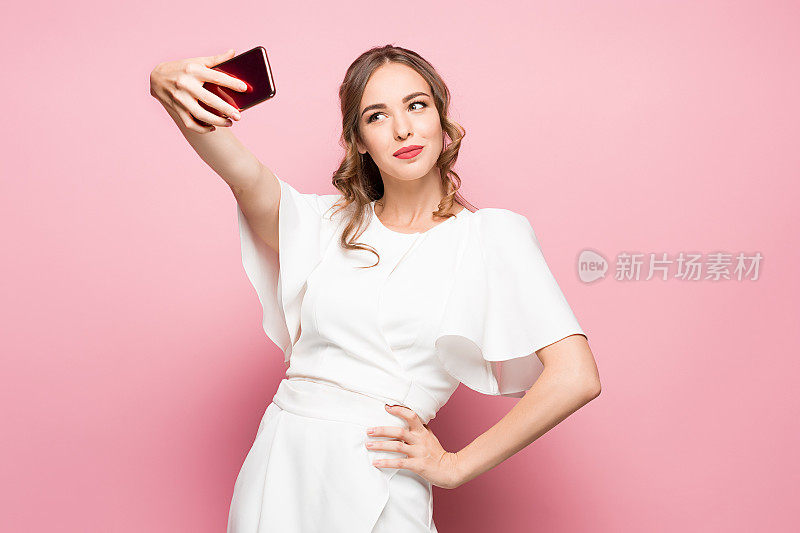 一个年轻迷人的女人用粉色背景的智能手机自拍的肖像