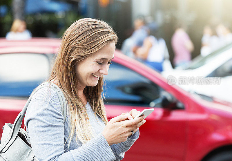 微笑的金发女人在路上发短信