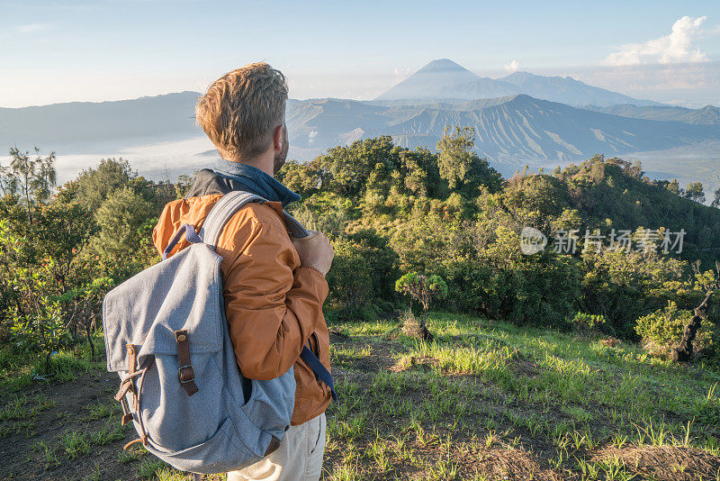 一名年轻人徒步旅行，从山顶眺望布罗莫火山，沉思火山景观