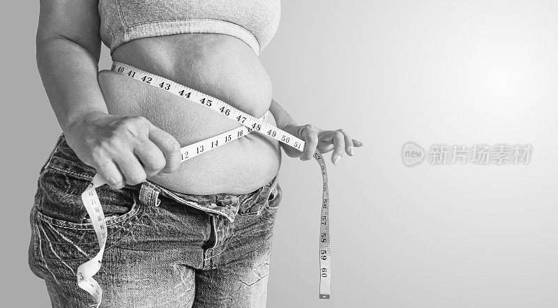 黑白相间的胖女人拿着测量尺。体脂百分比用卷尺测量脂肪。