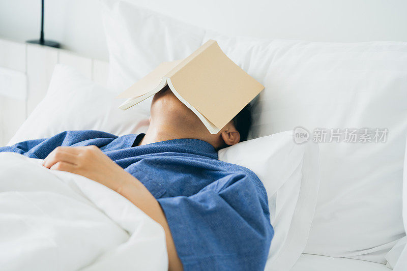 亚洲帅哥睡觉时看书。睡意导致睡眠。充足睡眠的概念。良好的睡眠