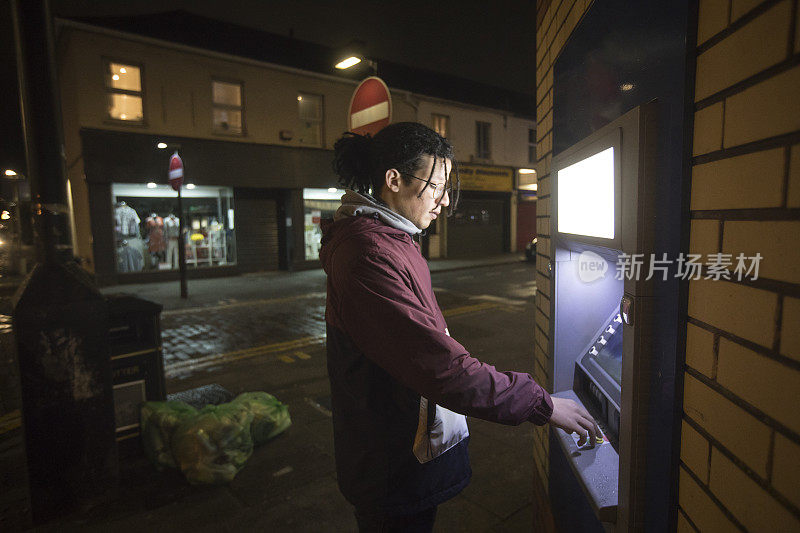 一名年轻人在城市大街上使用ATM机