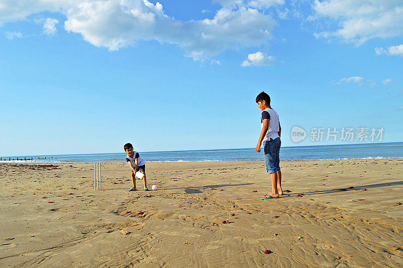 夏天的一天，两个孩子在海边的沙滩上打板球。