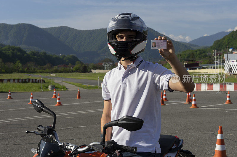 在摩托车上戴着头盔的年轻人正在出示驾驶执照