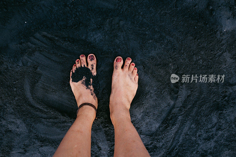 一个女人的脚踩在巴厘岛海滩的黑色沙滩上