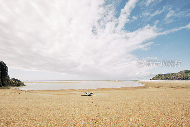 一个男人独自躺在沙滩上，伸开双臂，休息，远离这一切。