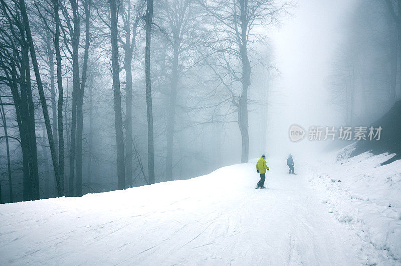 在一个雾蒙蒙的冬季森林里的滑雪坡上，滑雪者骑着认不出来的滑雪板