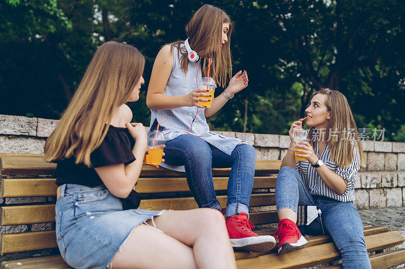 三个女朋友在长凳上喝着橙汁干杯