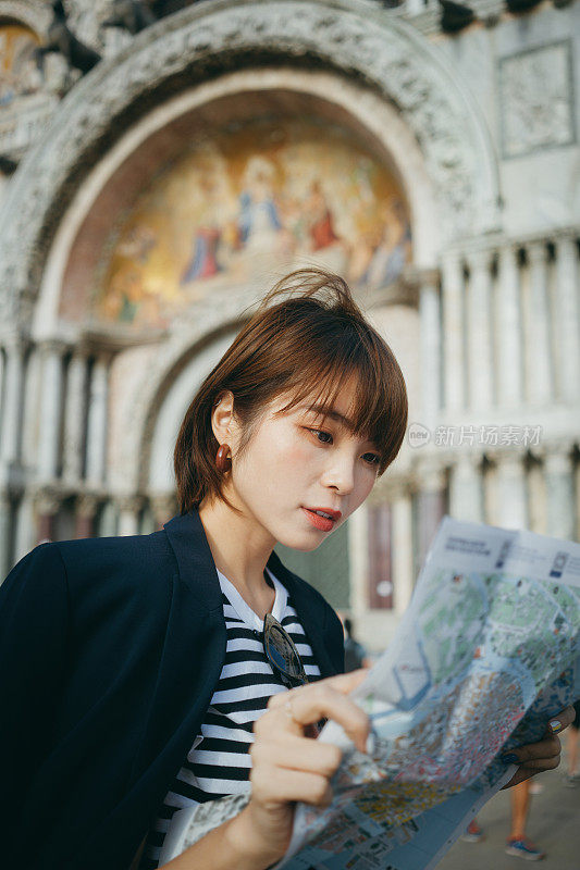 年轻的亚洲女性旅行者一边阅读地图，一边探索和走过意大利当地城市的街道