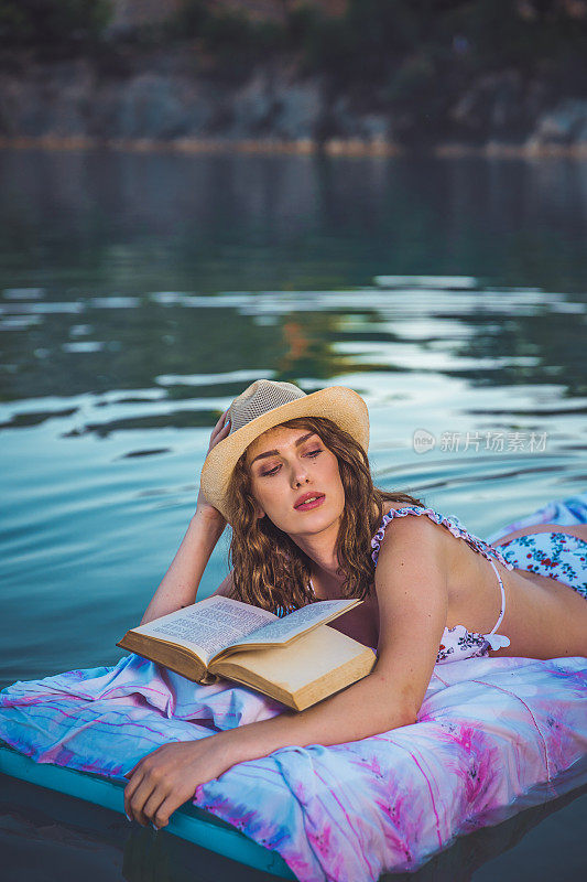 年轻快乐的女孩穿着比基尼在湖里游泳和读书