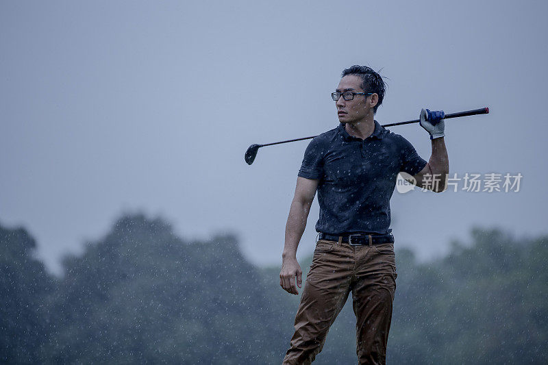 一个亚洲华人在雨天拿着他的高尔夫球杆在高尔夫球场上