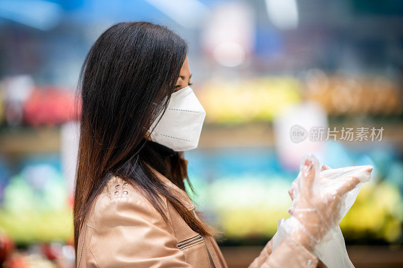 在Covid-19购物。Covid户外。新冠肺炎疫情期间，一名妇女戴着防护口罩，戴着防护手套，在超市果蔬区购物