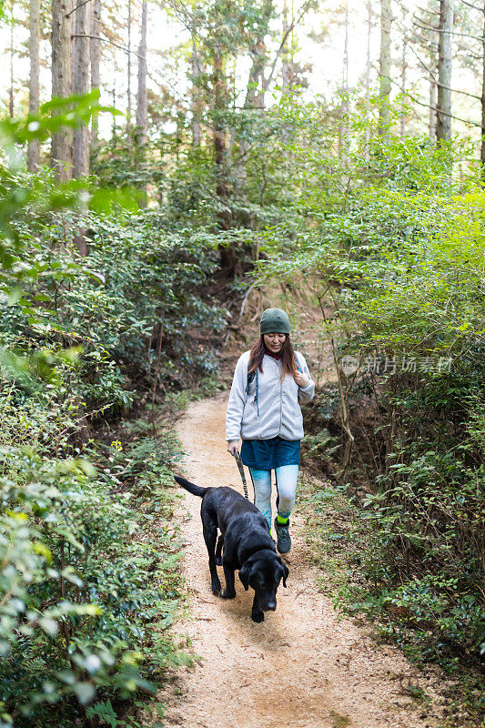 一个女人带着她的狗在山间森林的小路上徒步旅行