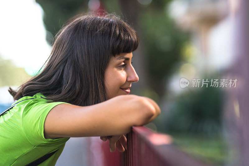 一个沉思的年轻女子在户外靠在一扇金属门上做着白日梦