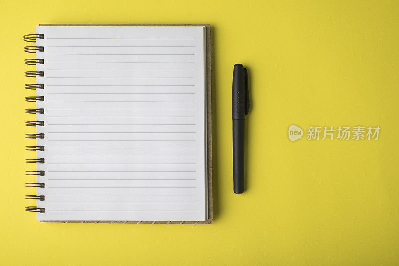 黄色背景上的空白笔记本和黑色钢笔
