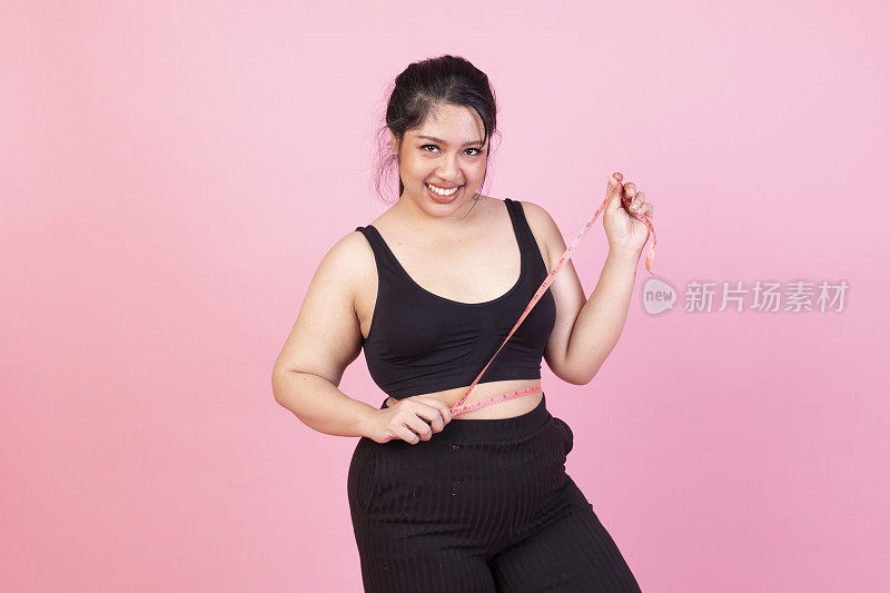 胖女人的身体测量孤立的粉红色背景。一个超重的女人在测量她腹部的脂肪。肥胖女性测量她的腹部在粉红色的背景。身体肥胖的妇女用卷尺收紧身体。