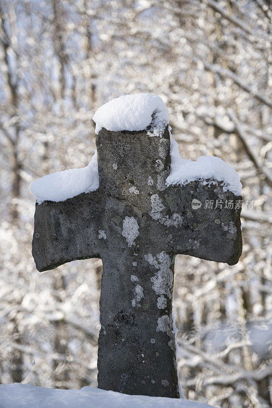 冬天下雪后的中世纪木板教堂外被雪覆盖的石头十字架