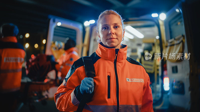 一名女性急救护理人员的肖像自豪地站在摄像机前，穿着能见度高的医用橙色制服，带有“急救人员”文本标志。成功的紧急医疗技术员或医生在工作。