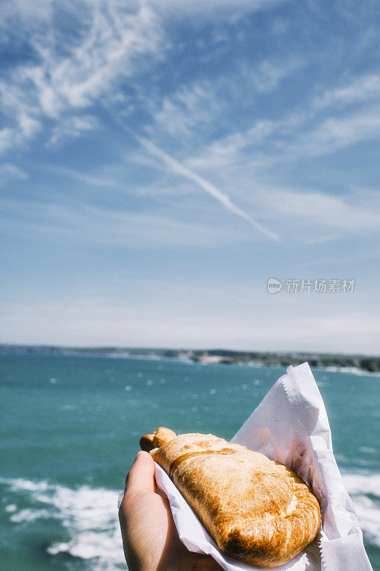 六月阳光明媚的纽基，一只手举着康沃尔馅饼在蓝色的海面上。