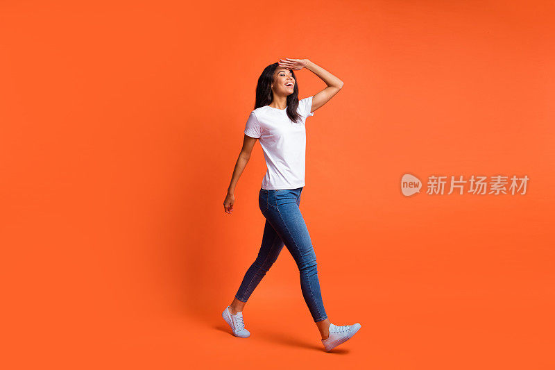 全长照片的女孩走看空的空间手掌前额穿白色t恤牛仔裤运动鞋孤立的橙色背景