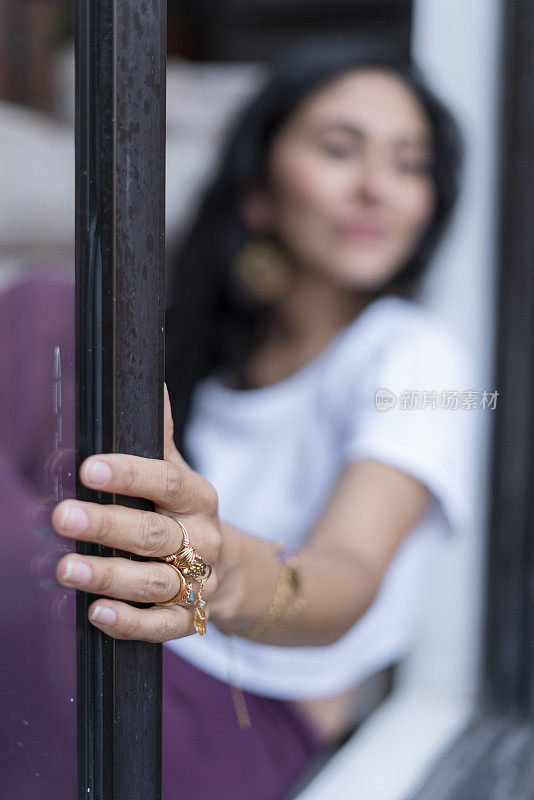 一名女子坐在客厅阳台的窗户上，一边望着别处，一边伸手抓住窗户，想着她的问题