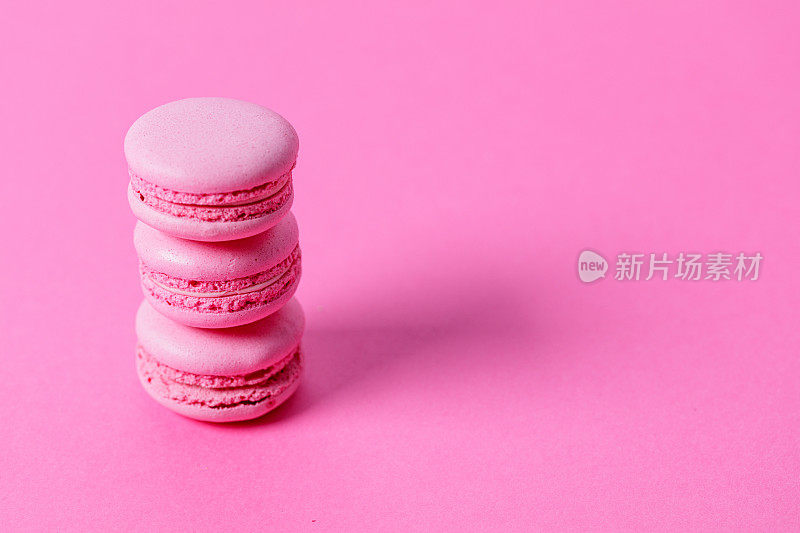 特写三个粉红色的杏仁饼干，粉红色的填充在粉红色的背景上