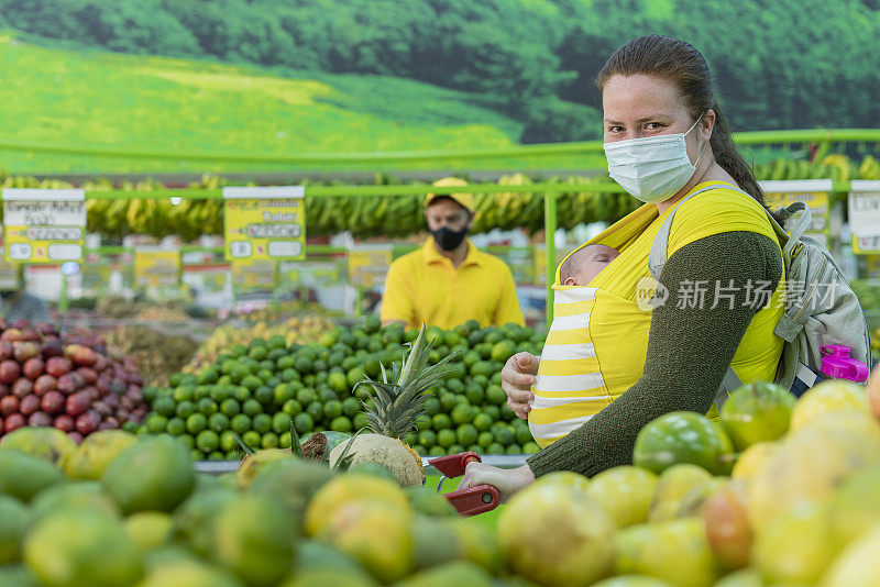 年轻的妇女抱着她的孩子在超市的水果和蔬菜选择他们的食物时看着相机的肖像