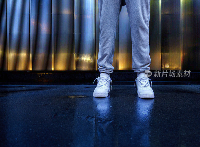 男子穿着白色运动鞋站在城市的户外，低角度