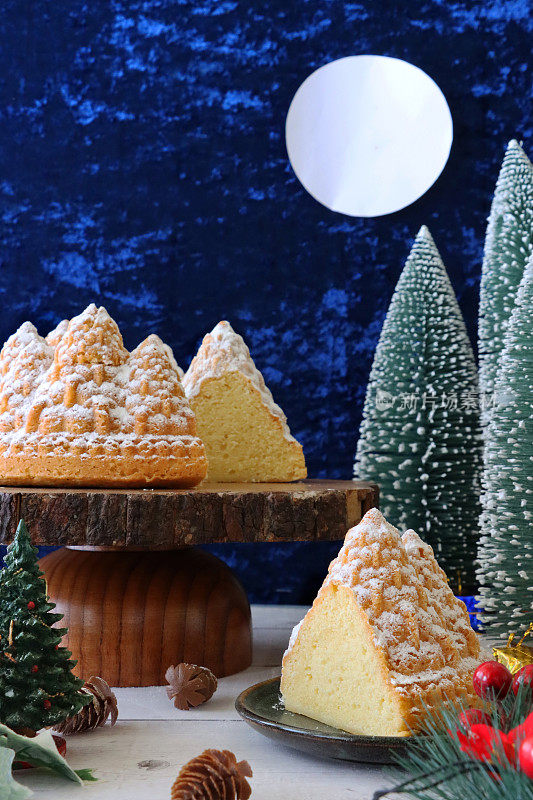 自制的切片，圣诞树形状，柠檬毛绒绒的Bundt蛋糕，柠檬味的环状海绵覆盖着糖霜，木制蛋糕架被圣诞树环绕，蓝色背景与满月