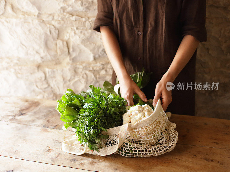 女人拿着装有蔬菜和草药的网袋