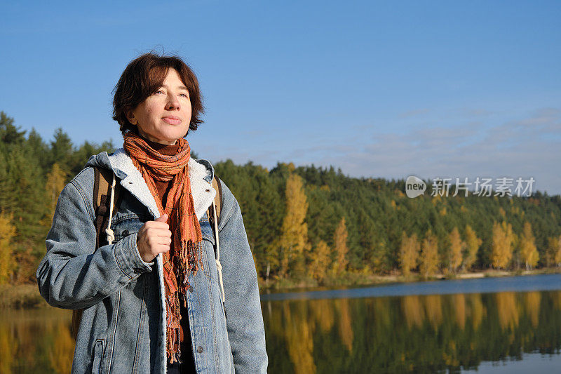 在阳光明媚的秋日自然公园的湖岸漫步的女人的腰部肖像